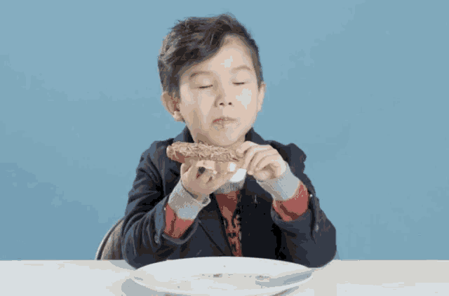 a young boy sitting at a table eating a sandwich