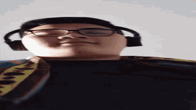 a man wearing glasses and headphones looks at the camera with his eyes closed