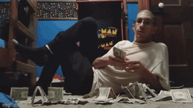 a man is laying on the floor surrounded by money and a pac man poster
