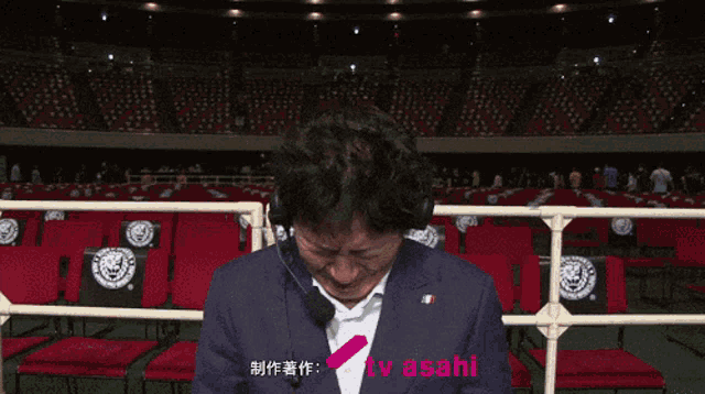 a man wearing a suit and headphones is crying in front of a tv asahi sign