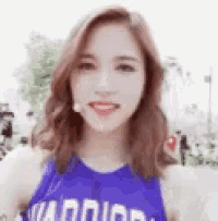 a woman wearing a blue tank top with the word warrior on it is smiling .