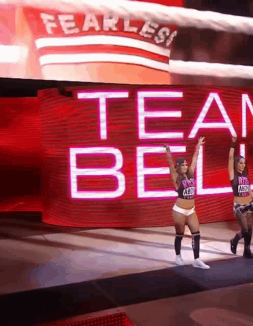 two women are walking in front of a large screen that says fearless team bell