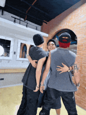 three men are hugging each other in a room with the word zky on the bottom right