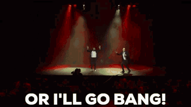 two men are dancing on a stage in front of a crowd with the words `` or i 'll go bang '' above them .