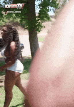 a woman in white shorts is walking in a park with now that 's tv written on the bottom right