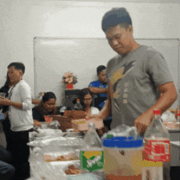 a man in a grey shirt with a lightning bolt on it stands in front of a table full of food and drinks
