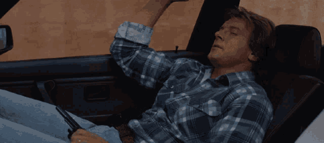a man in a plaid shirt sits in a car