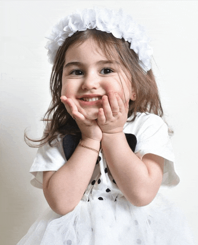 a little girl wearing a white dress and a white flower crown