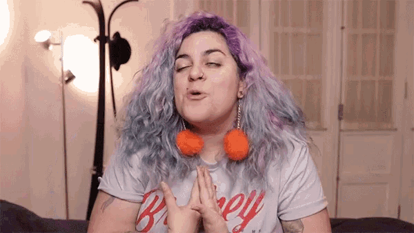 a woman with purple hair is sitting on a couch with her eyes closed and making a funny face .