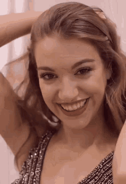 a woman is smiling and holding her hair while wearing a sequined dress .