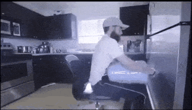 a man sitting in a chair in a kitchen with a laptop on his lap