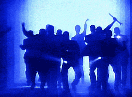 a group of people are dancing in a dark room with blue lights behind them