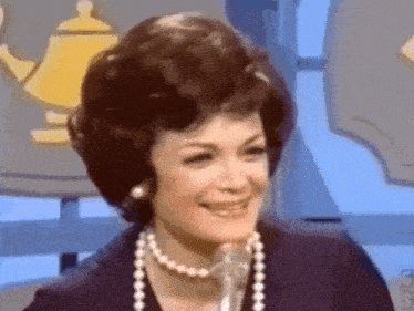 a woman wearing a pearl necklace and earrings is smiling into a microphone .