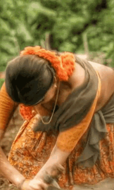 a woman in a saree is kneeling down in the dirt and working in a garden .