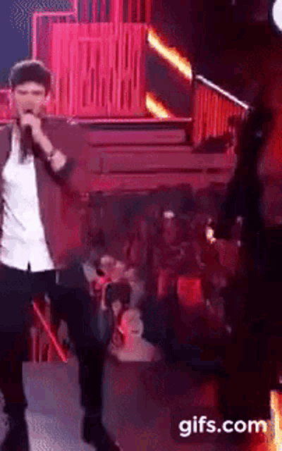 a man singing into a microphone on a stage with a gifs.com watermark on the bottom