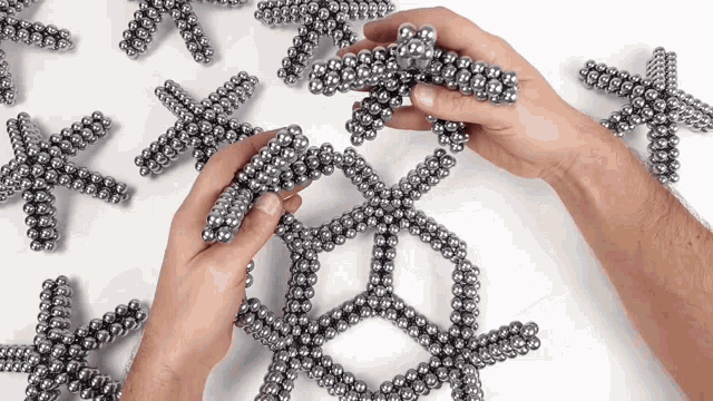 a person is playing with a bunch of metal balls on a white surface