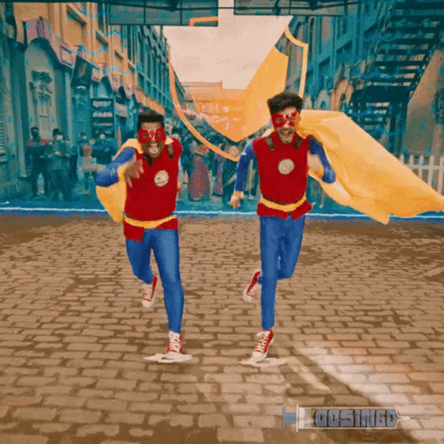 two men in superhero costumes are running on a brick road