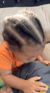 a little boy is sitting on a couch with his eyes closed and his hair in braids .