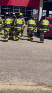 a group of firefighters are walking towards a fire station .