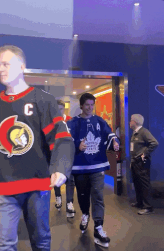 a man in a toronto maple leafs jersey walks down a hallway with other people
