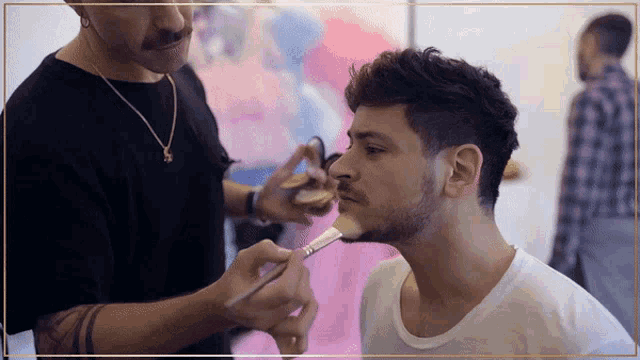 a man applying makeup to another man 's face with a brush