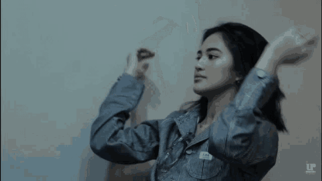 a woman in a denim jacket is stretching her arms in front of a white wall .