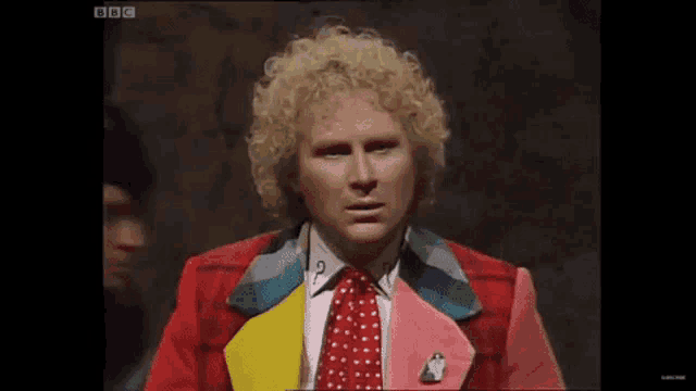 a man with blonde curly hair is wearing a red jacket and tie .