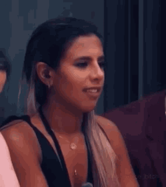 a woman in a black tank top is smiling while sitting in a room with other people .