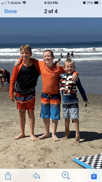 a phone screen shows a picture of three boys on the beach with the time 6:03 pm