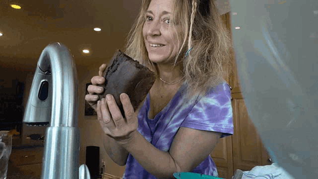 a woman in a purple tie dye shirt holds a piece of chocolate