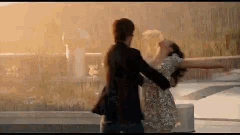 a man and a woman are dancing together in front of a fountain in the rain .