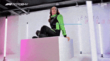 a woman in a green and black outfit is sitting on a cube in front of a sign that says academy
