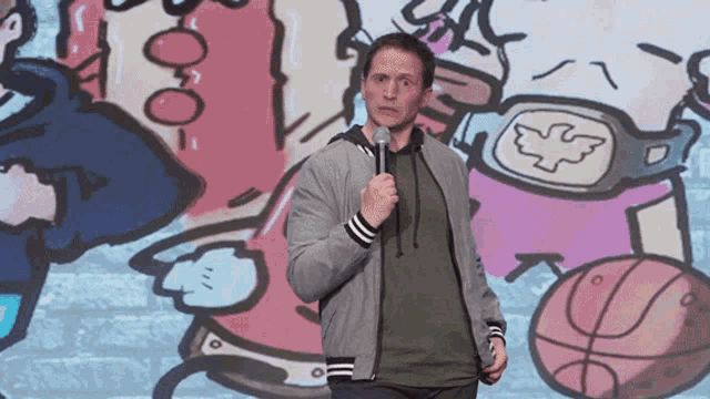 a man is holding a microphone in front of a wall with drawings on it