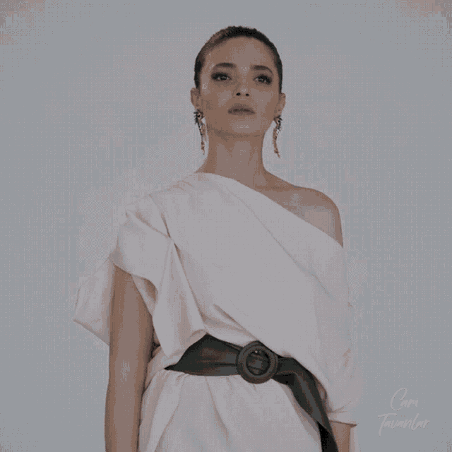 a woman wearing a white dress with a green belt and earrings stands in front of a sign that says cam tavanlar