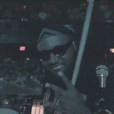 a man wearing sunglasses and a bandana is holding a microphone in front of a crowd .