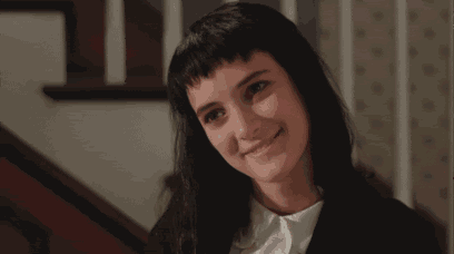 a woman with black hair and a white shirt is smiling while standing on a set of stairs .