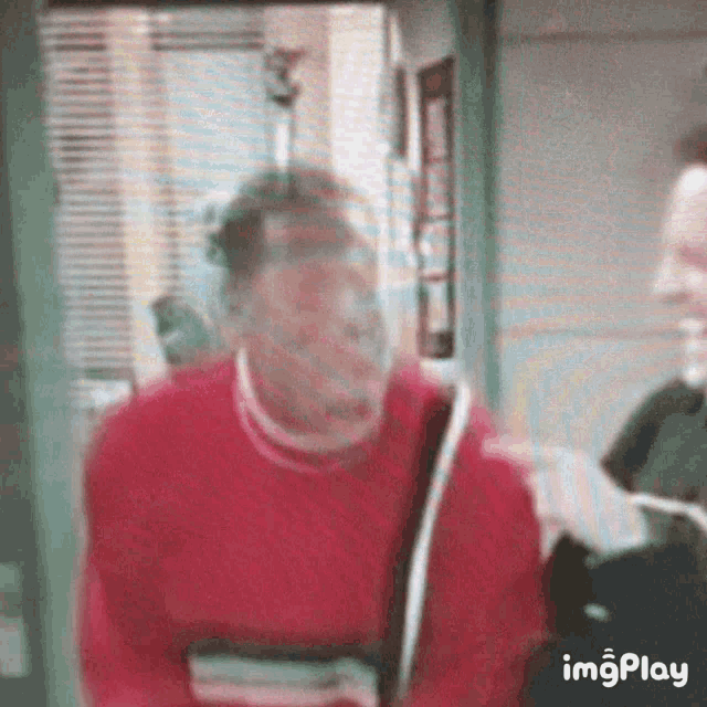 a blurry picture of a man in a red sweater talking to another man in a room .