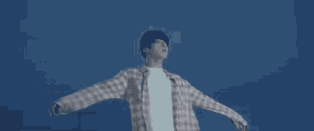 a young man in a plaid shirt is standing with his arms outstretched in the dark .