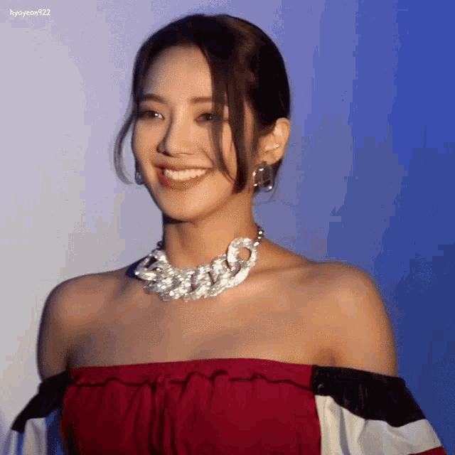 a woman wearing a red off the shoulder top and a silver necklace