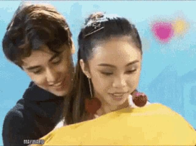a boy and a girl are hugging each other and the girl is holding a yellow pillow