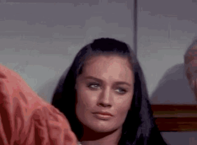 a woman with long black hair is looking at the camera with a man behind her .