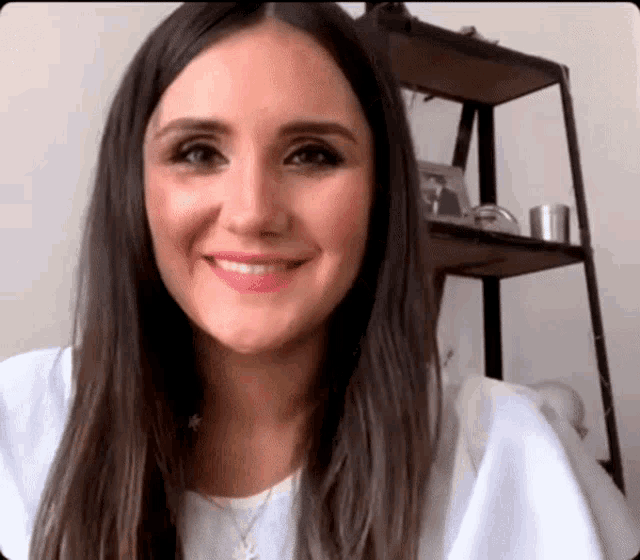 a woman with long dark hair is smiling in front of a shelf
