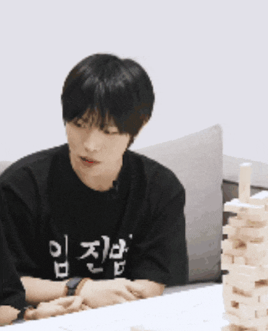 a man wearing a black shirt with korean writing on it sits at a table with a stack of wooden blocks