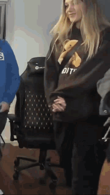 a woman in a teddy bear sweatshirt is standing next to a chair .