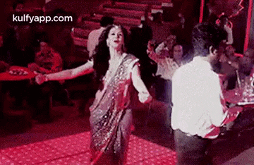 a woman in a sari is dancing with a man in a white shirt on a dance floor .