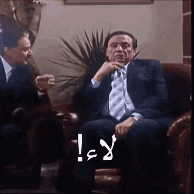 a man in a suit and tie is sitting on a couch talking to another man