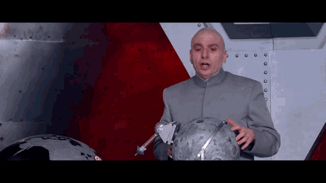 a bald man in a gray suit holds a globe