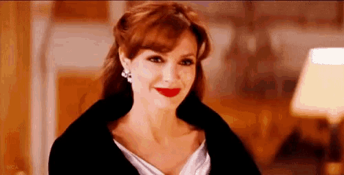 a woman wearing a white dress and a black coat is smiling and looking at the camera .
