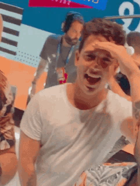 a man in a white shirt is laughing and covering his face