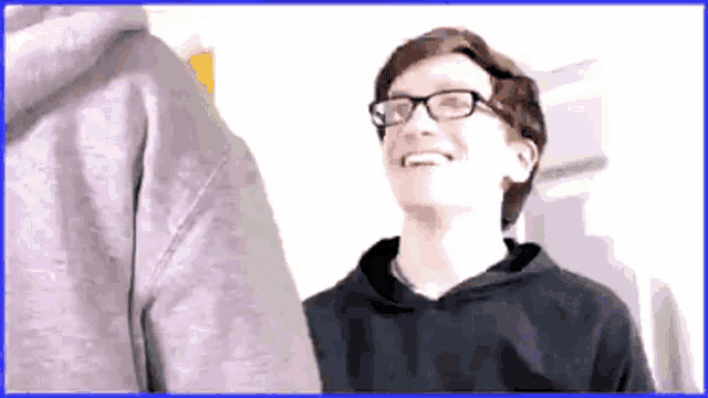 a young man wearing glasses and a hoodie smiles